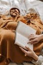 Hands holding a book surrounded by string lights and a warm blanket for a cozy reading vibe.